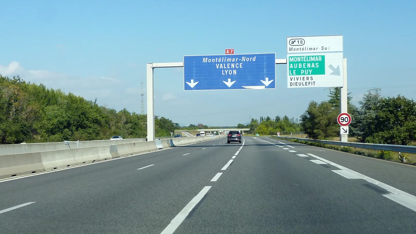 Autoroute A7 à deux voies sous un ciel bleu, avec un portique de signalisation vers Valence et Lyon et une voiture au loin