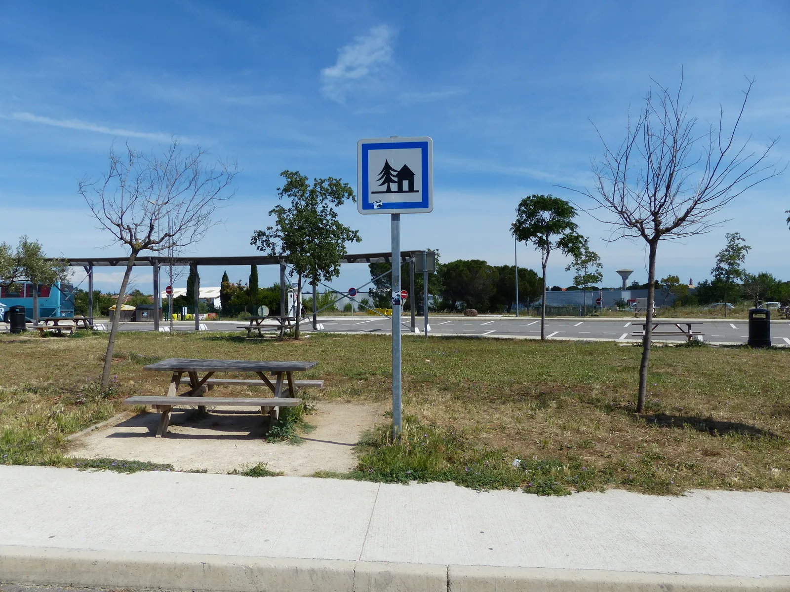 Table de pique-nique en bois sous un panneau bleu d'aire de repos, sur une aire de l'autoroute A9 dans le Gard