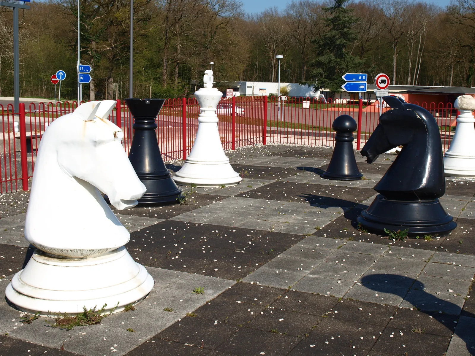 Jeu d'échecs géant avec des pièces noires et blanches sur un damier au sol, sur une aire de repos de l'autoroute A6